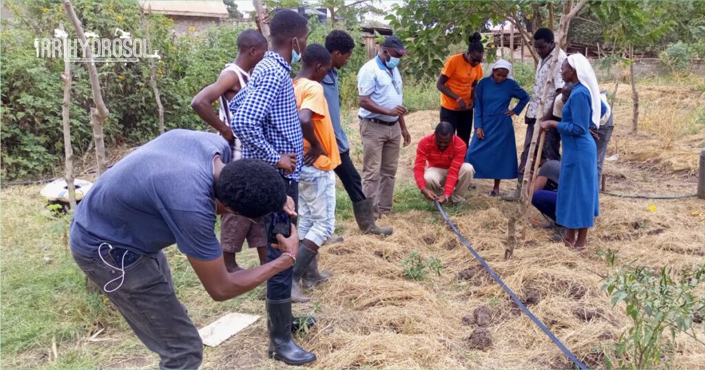 Group of Kenya Institute of Organic Farming (KIOF) students participating in outdoor agricultural training workshop with Irrihydrosol instructor demonstrating modern farming techniques